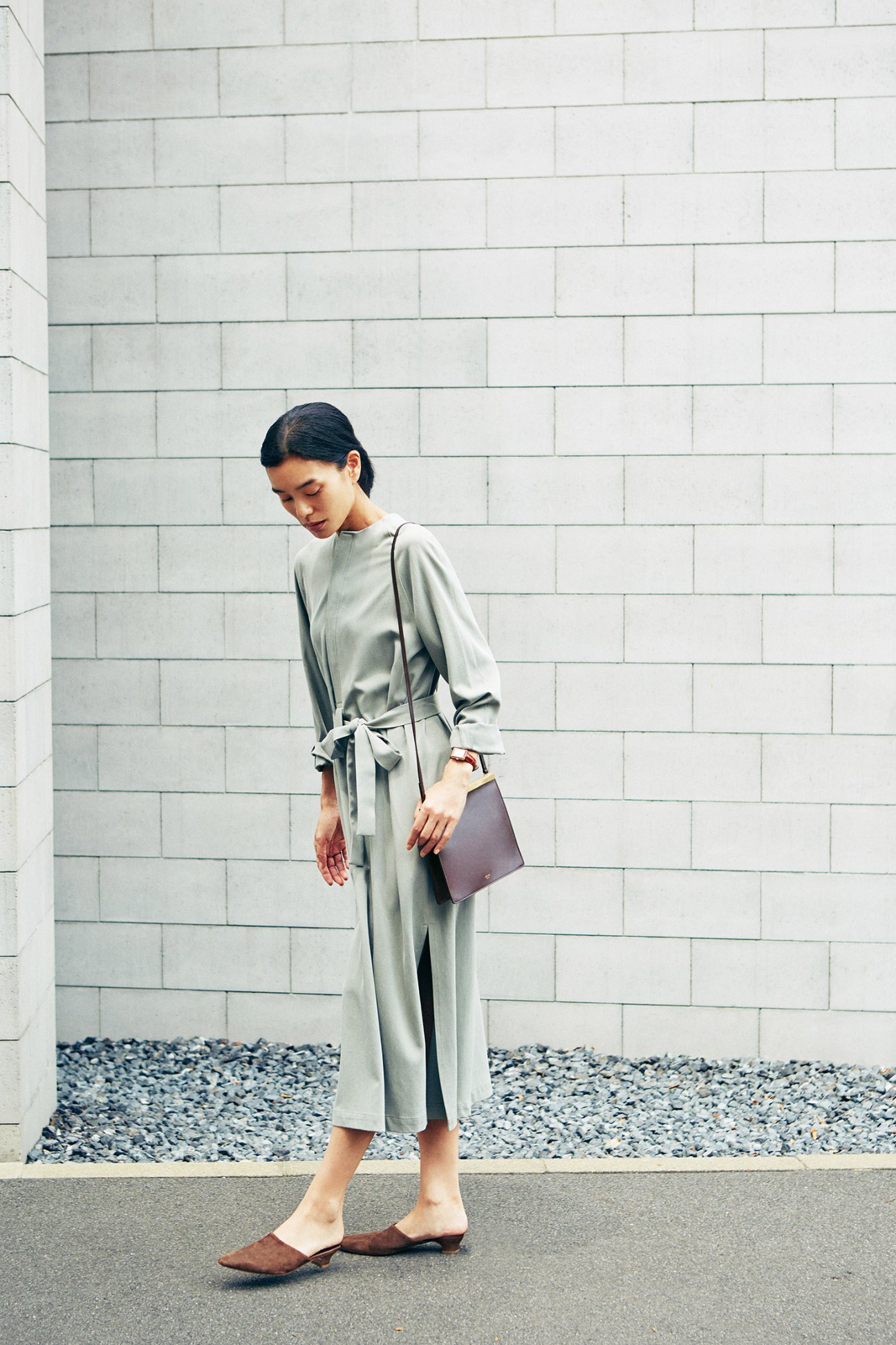 Woman wearing a sage green dress by Seya with brown Mansur Gavriel shoes and Céline bag against a white brick wall.