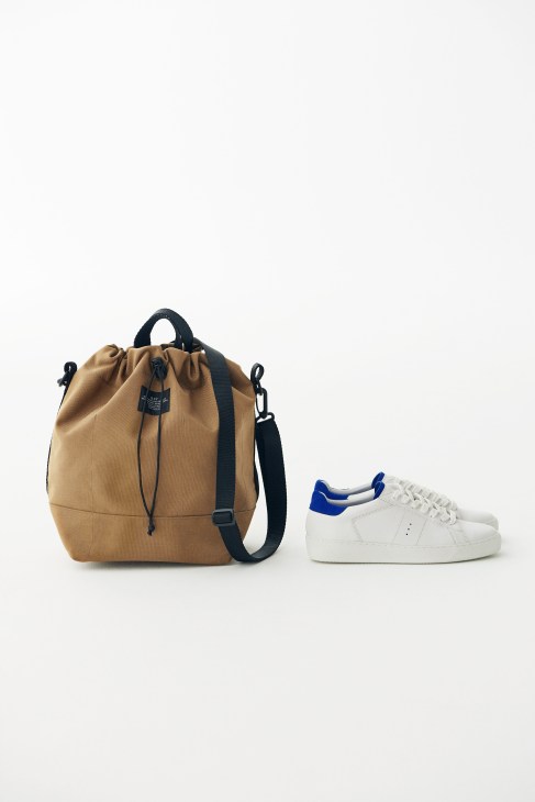 Tan canvas backpack with black straps and white sneaker with blue heel detail.