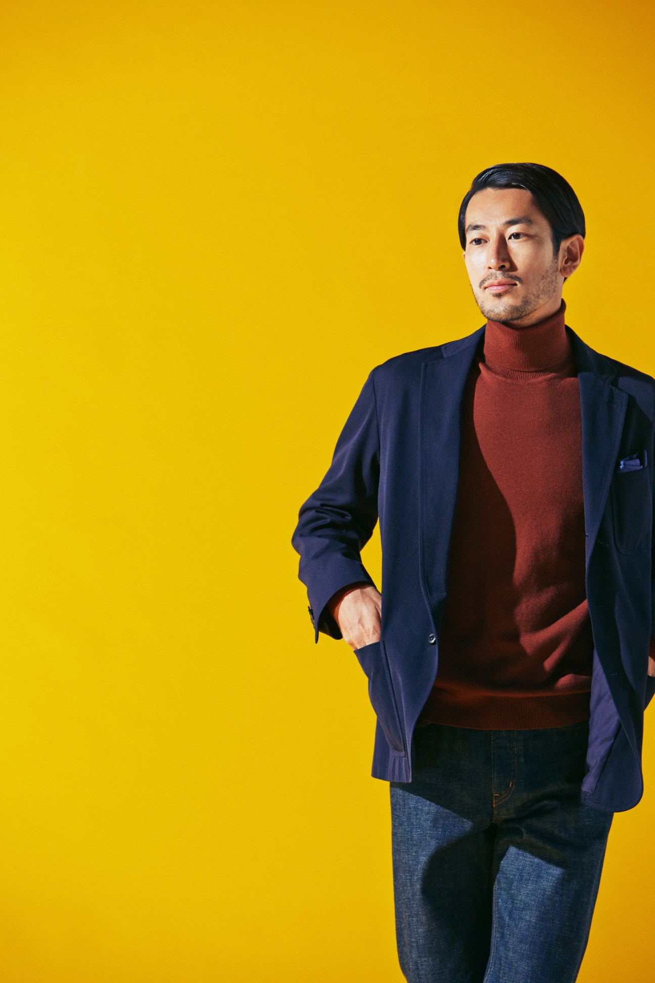 Man wearing navy Comoli jacket, burgundy Pal Zileri rollneck jumper, and Louis Vuitton jeans against yellow background