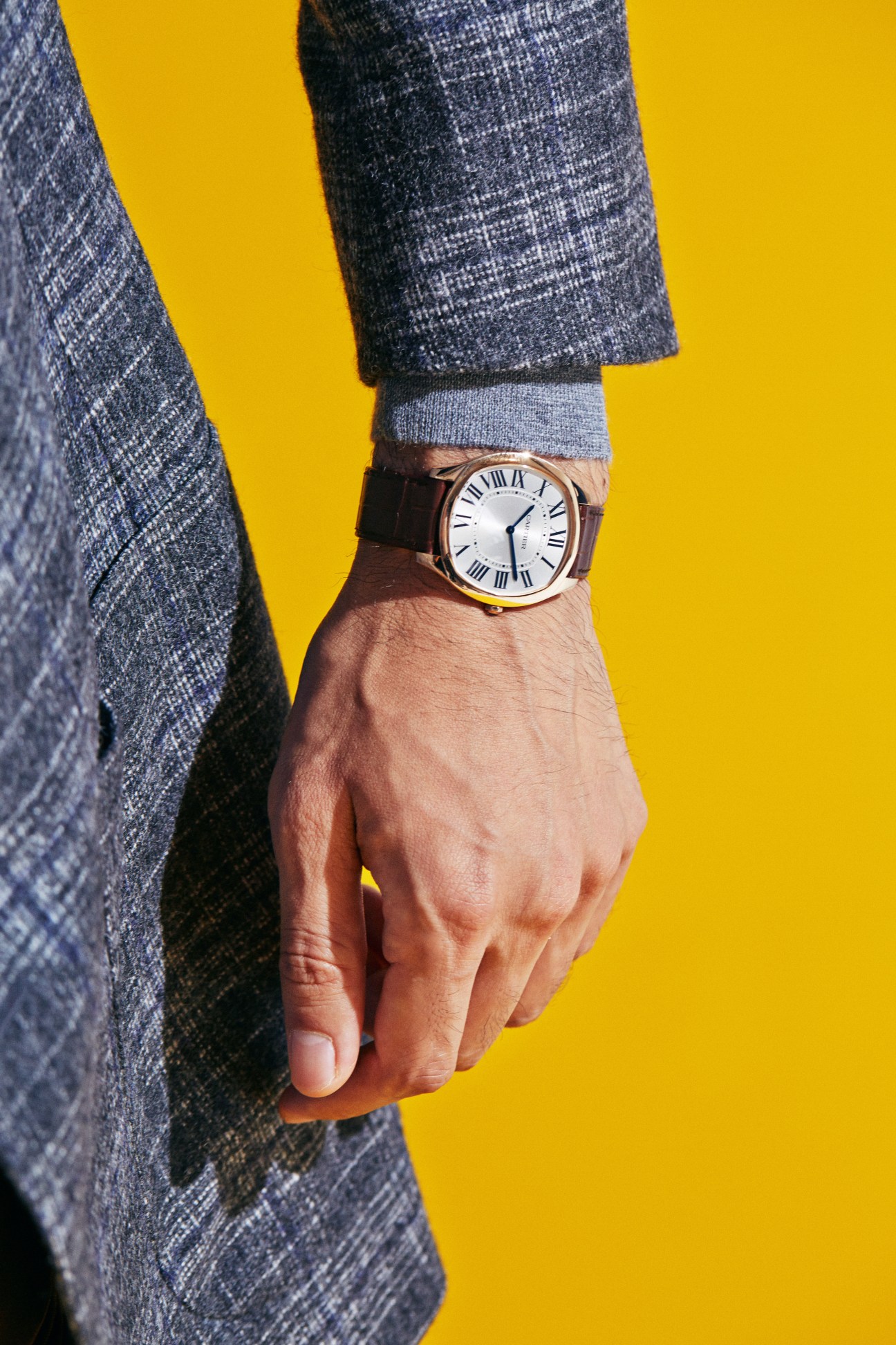 Close-up of man's hand wearing Cartier watch with Roman numerals against yellow background