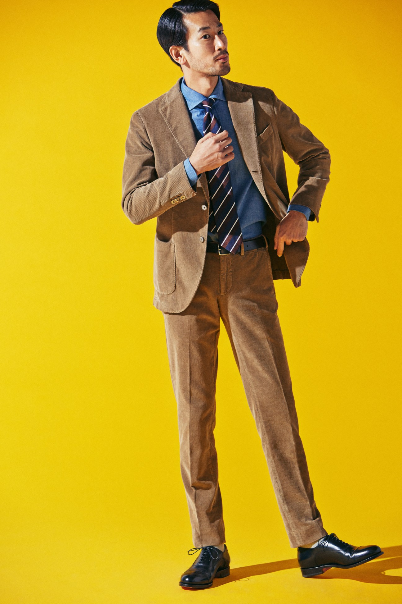 Man in brown corduroy suit with blue shirt and striped tie against yellow background