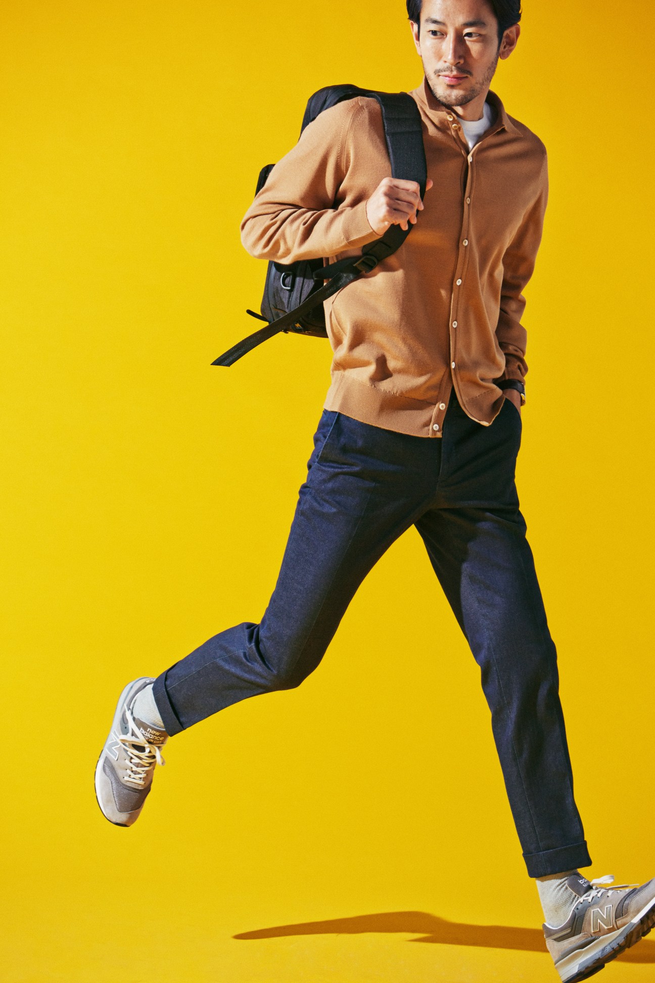 Man in mid-stride wearing John Smedley cardigan, Incotex jeans, and New Balance trainers with Hobo bag