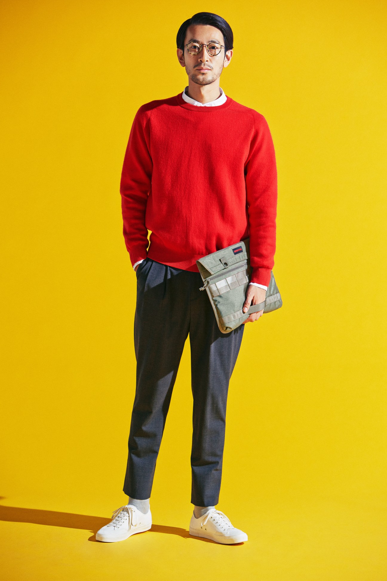 Man in red jumper and dark trousers holding a bag against yellow background