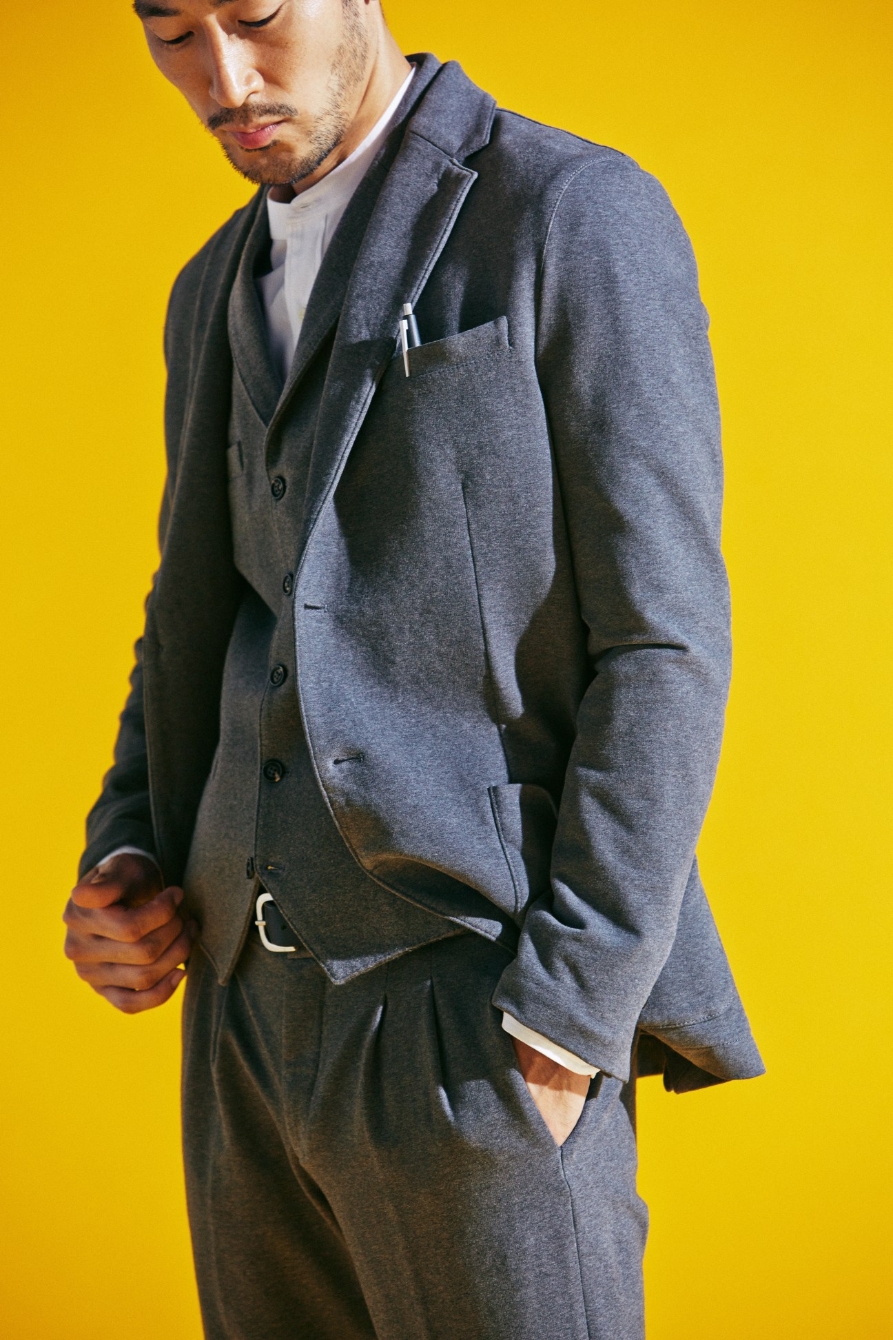 Man in grey three-piece suit by Circolo 1901 with white shirt, belt by APC, and Lamy pen against yellow background