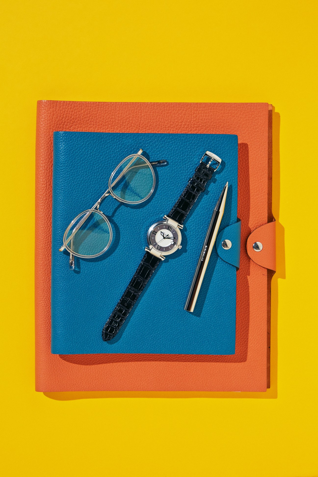 Business accessories including glasses, watch, and pen arranged on colorful leather notebook covers