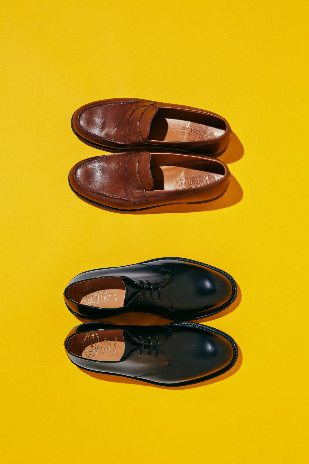 Two pairs of leather dress shoes on yellow background - brown JM Weston loafers and black Church's oxfords