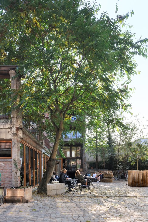 People relaxing in outdoor seating area under shade with modern industrial architecture