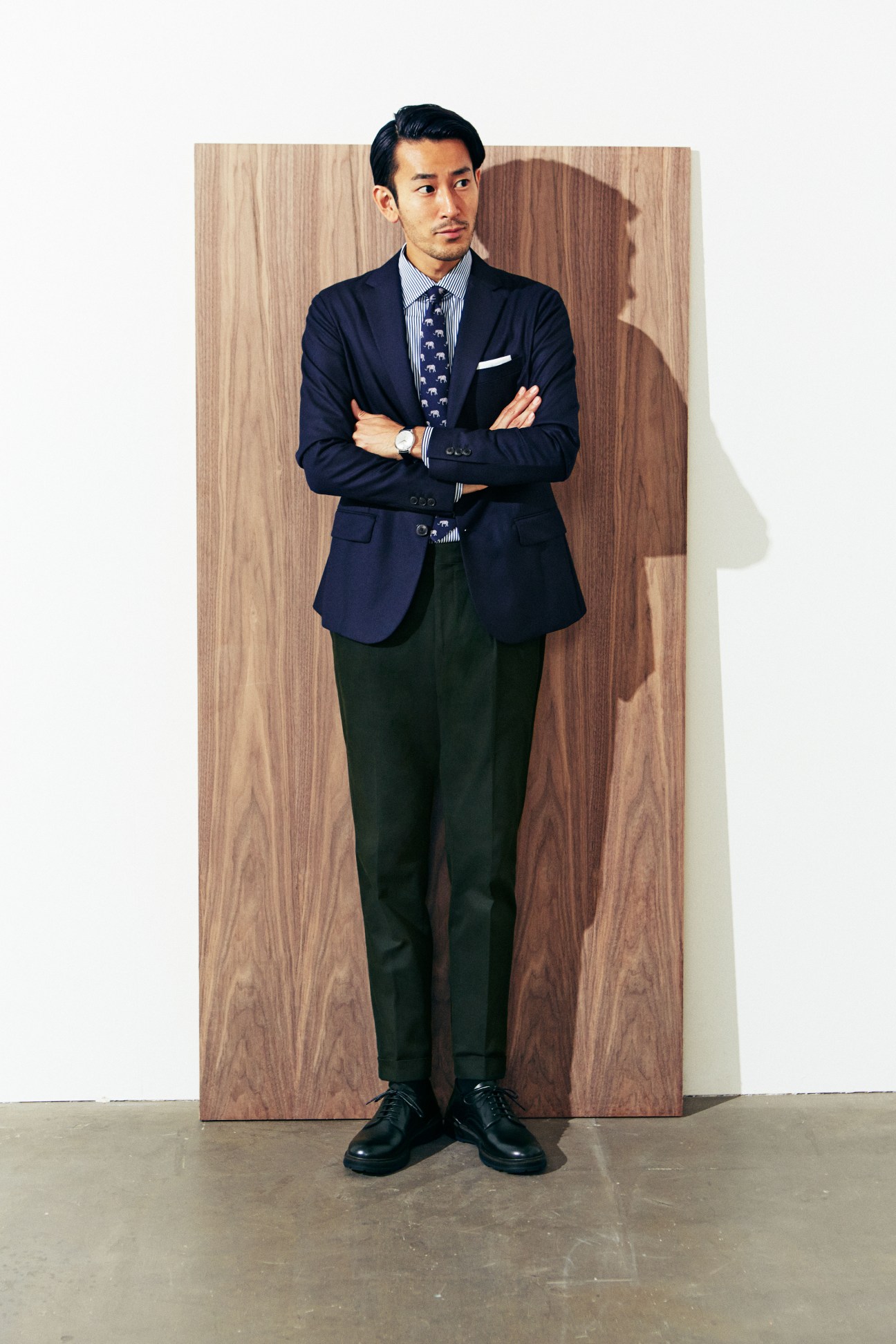 Man in navy Emporio Armani jacket, striped shirt and patterned tie standing with crossed arms.