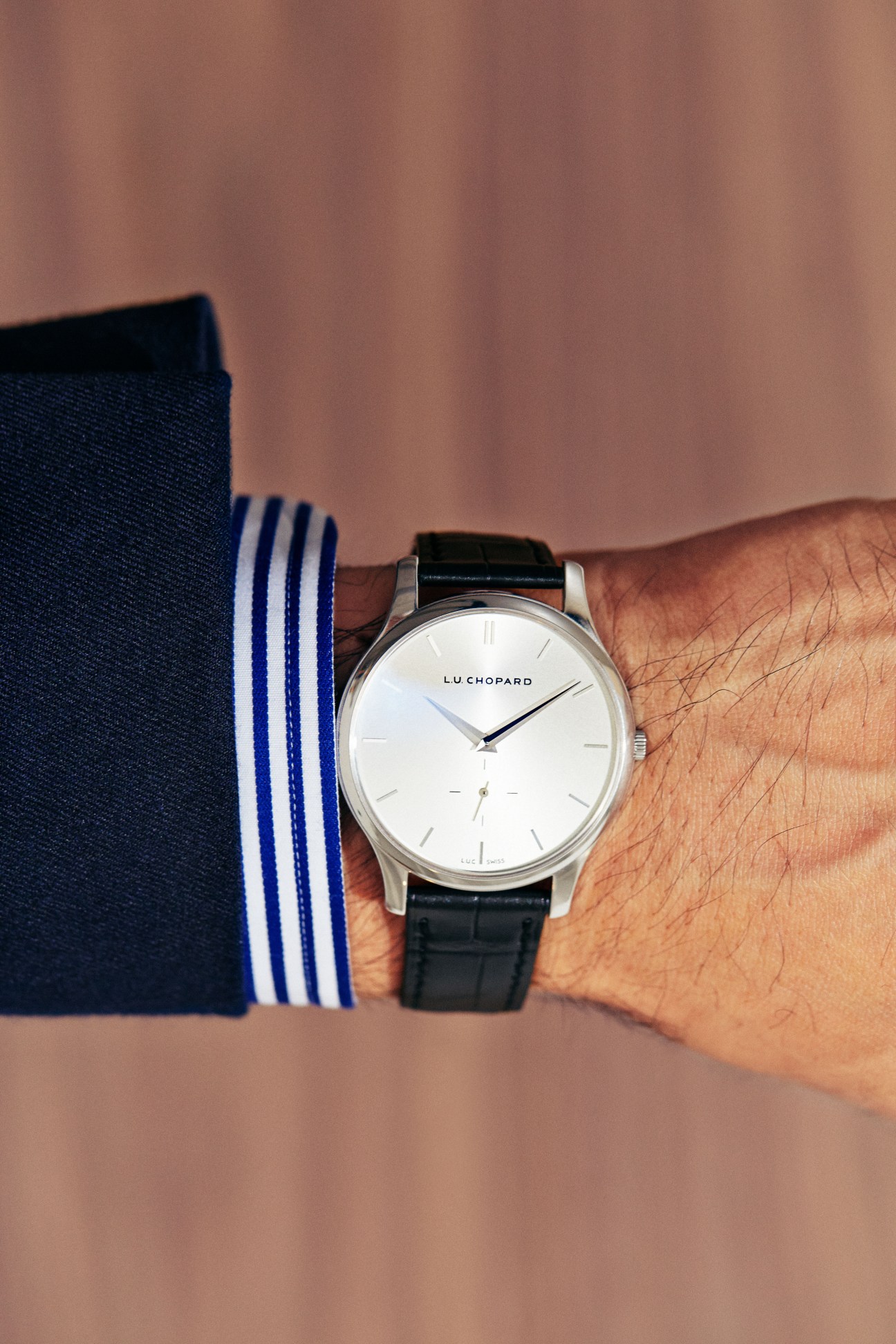 Chopard watch with white dial and black leather strap worn on wrist with striped navy sock visible.