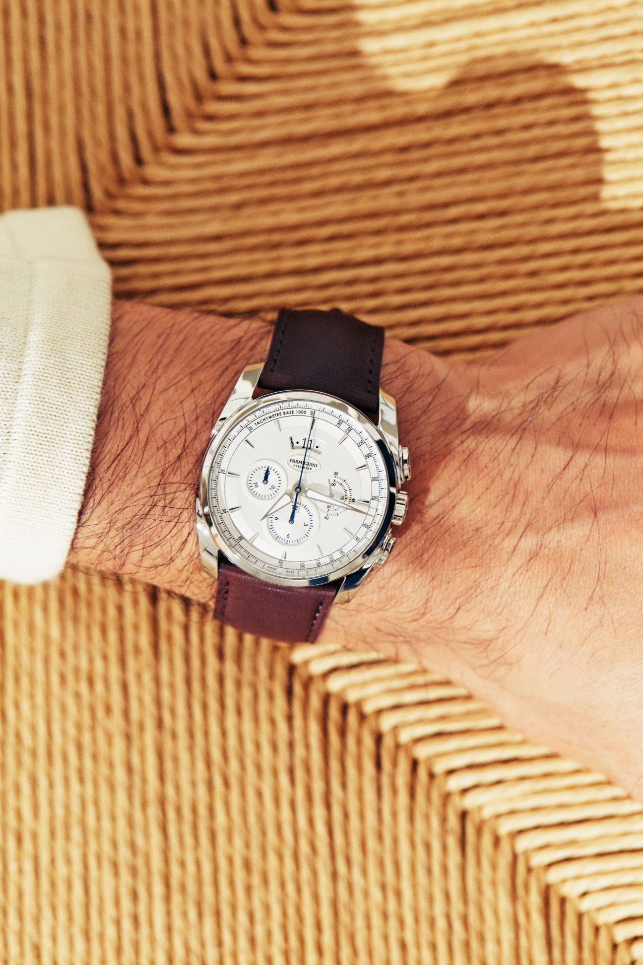 Parmigiani Fleurier chronograph watch with white dial and burgundy leather strap on wrist wearing cream and tan striped knitwear.