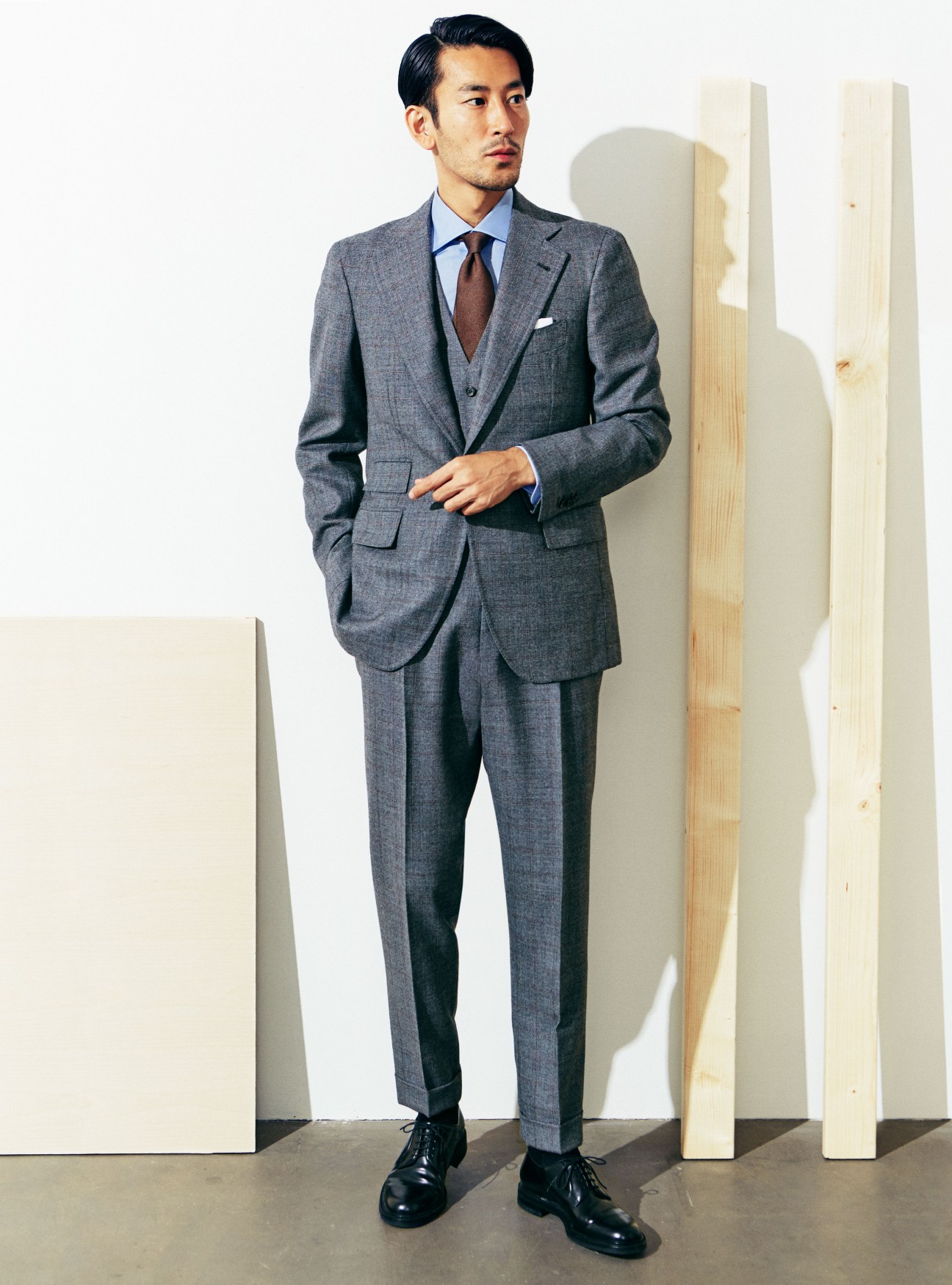 Man in grey Orazio Luciano suit with Bagutta shirt and Cocon tie standing against wooden panels.