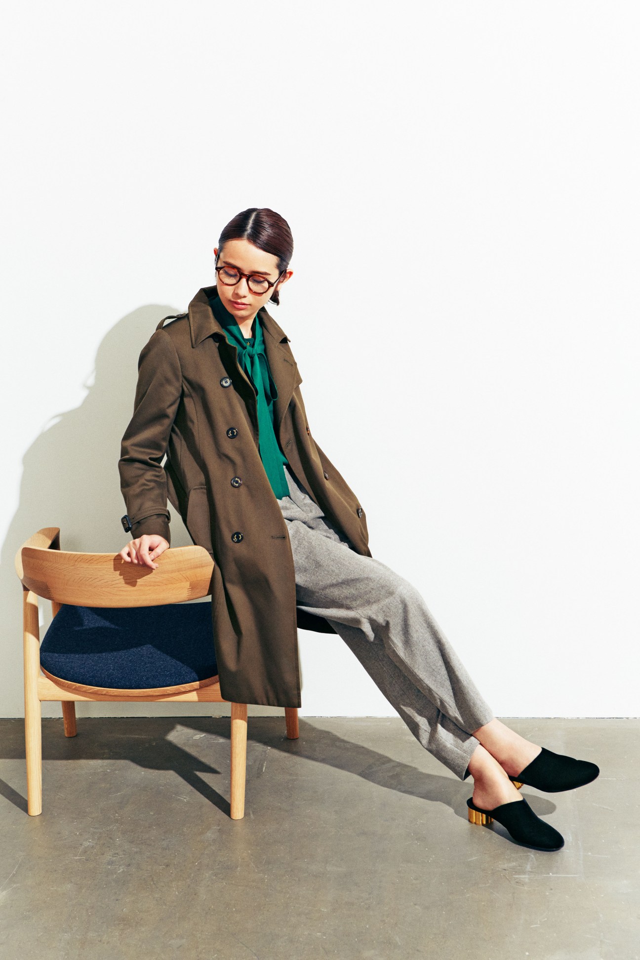 Woman in brown coat and grey trousers sitting on wooden chair with blue cushion
