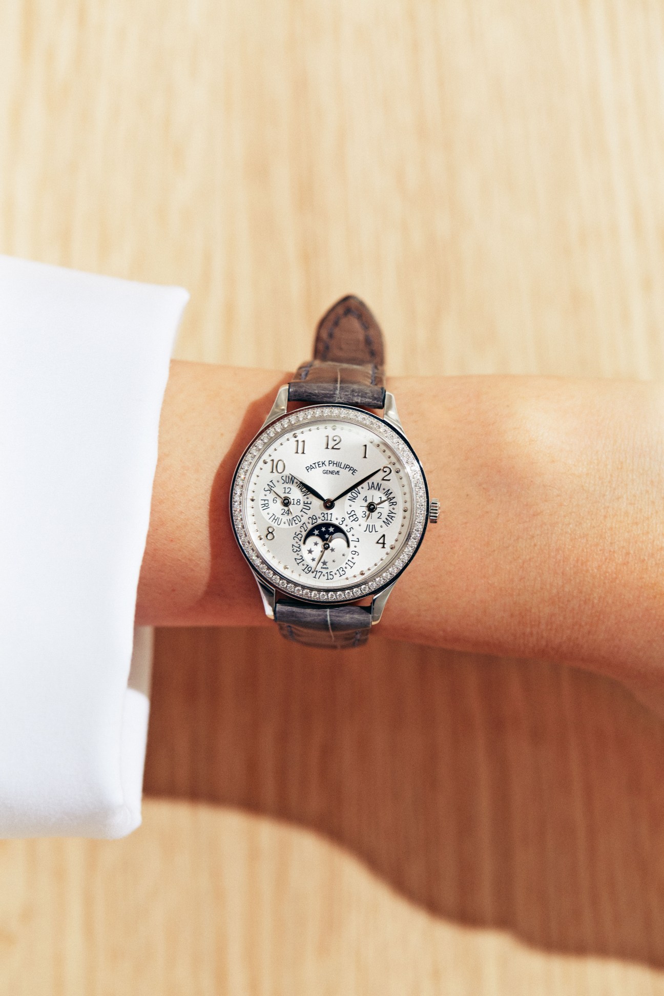 Patek Philippe watch with white dial and diamond bezel on brown leather strap worn on wrist.