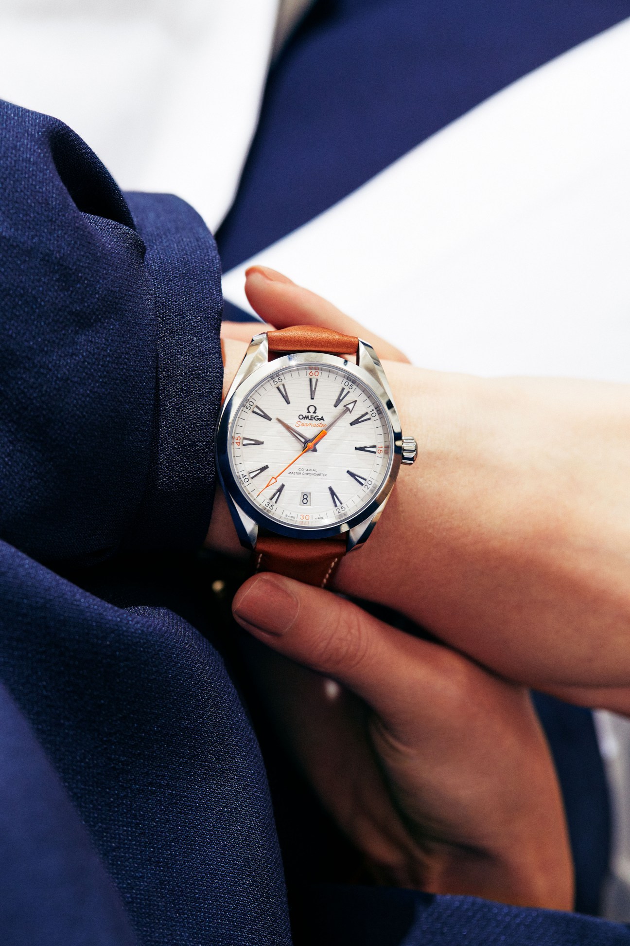 Omega watch with white dial and brown leather strap worn on wrist against navy blue fabric