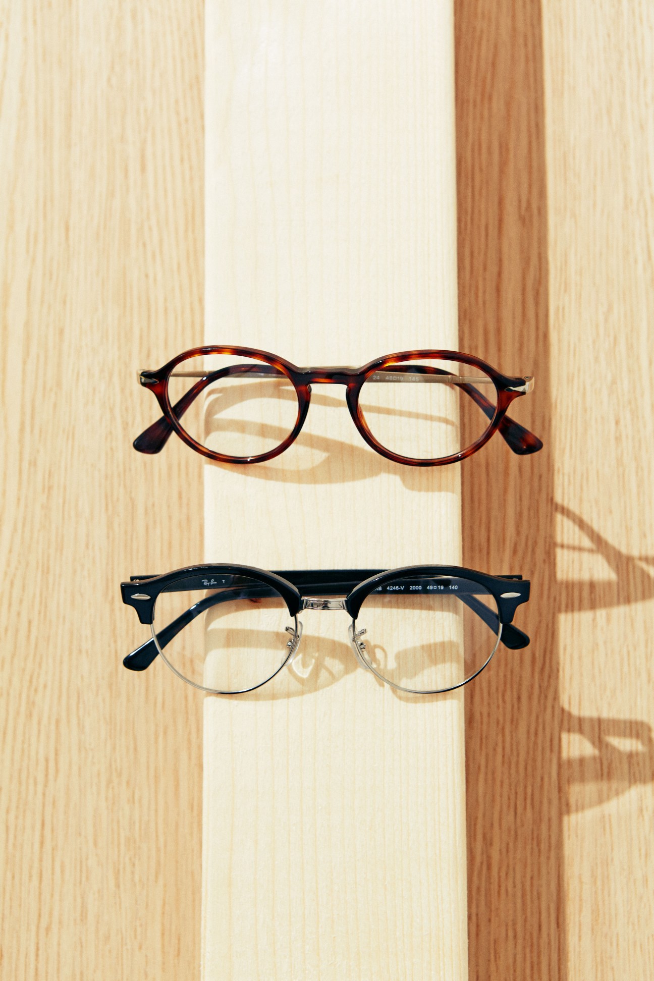 Tortoiseshell Persol glasses above black Ray-Ban clubmaster-style glasses on wooden background