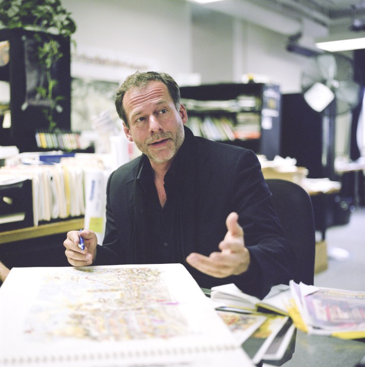 Alexandros Washburn, director of the urban design division, gestures while discussing plans at a table covered with maps and drawings in an office studio.