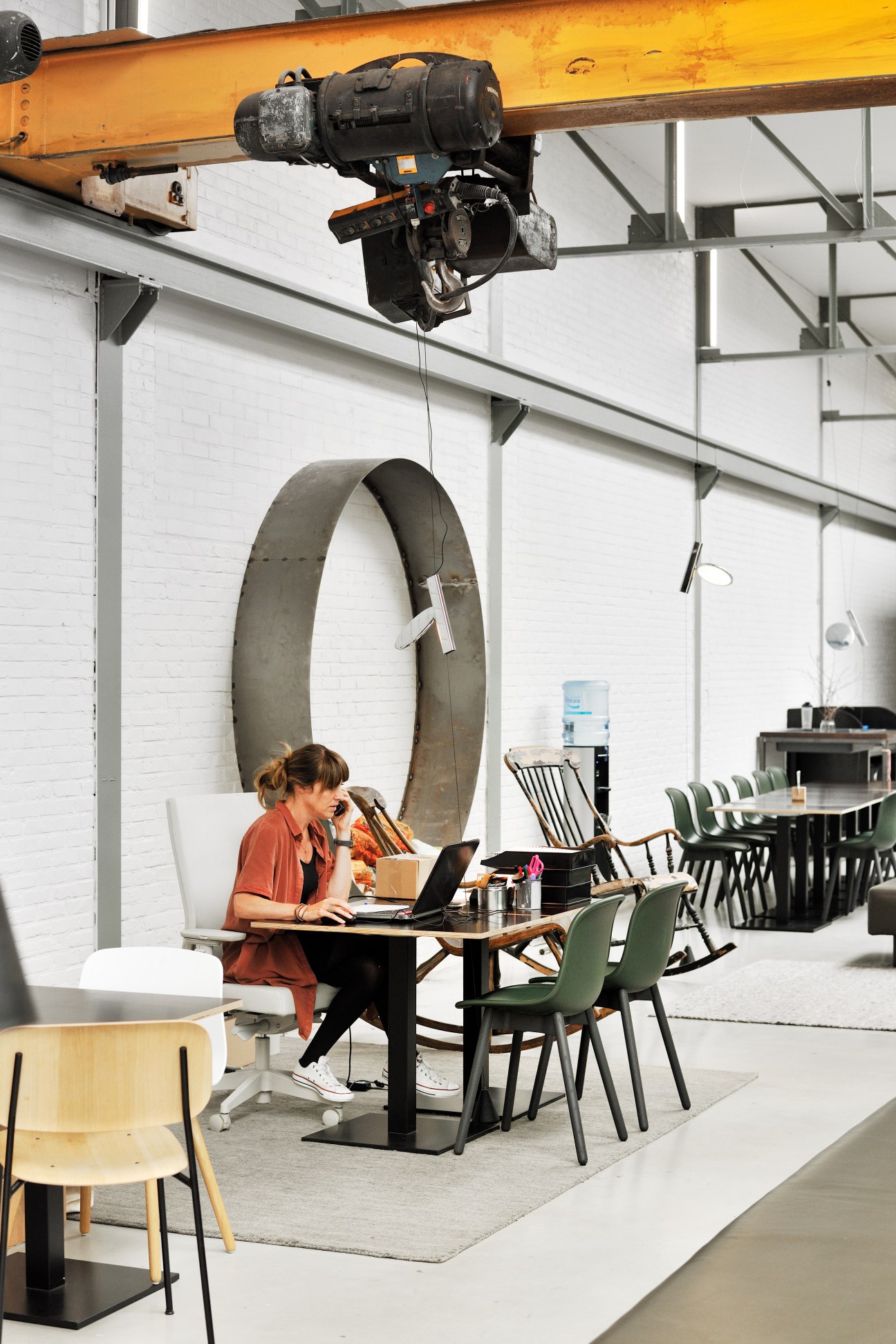 Woman working at laptop in modern office with industrial crane overhead and large sculptural letter O in background