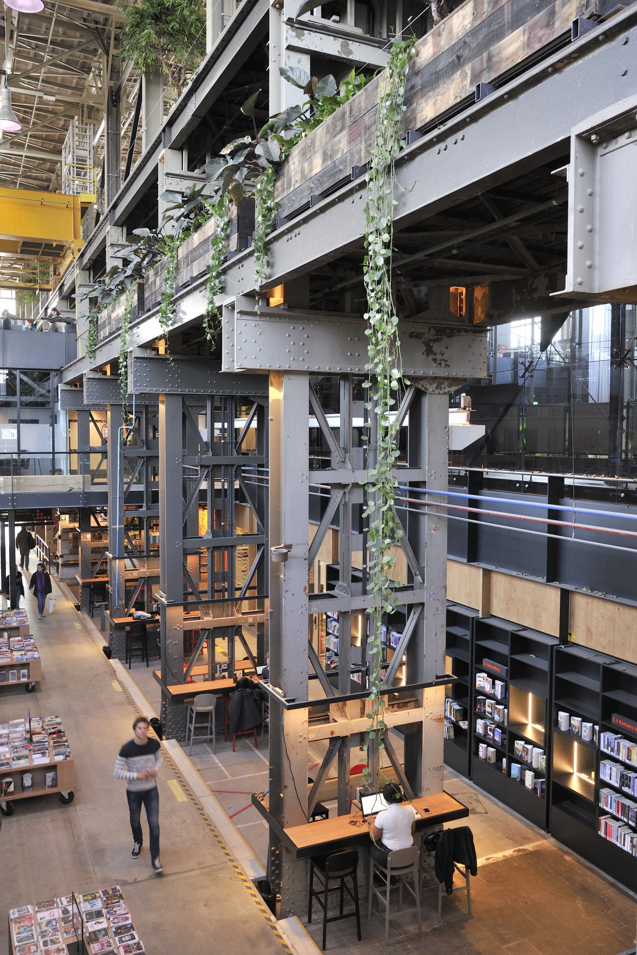 Industrial interior of LocHal with steel girders, ivy cascading from above, and wooden café seating below.