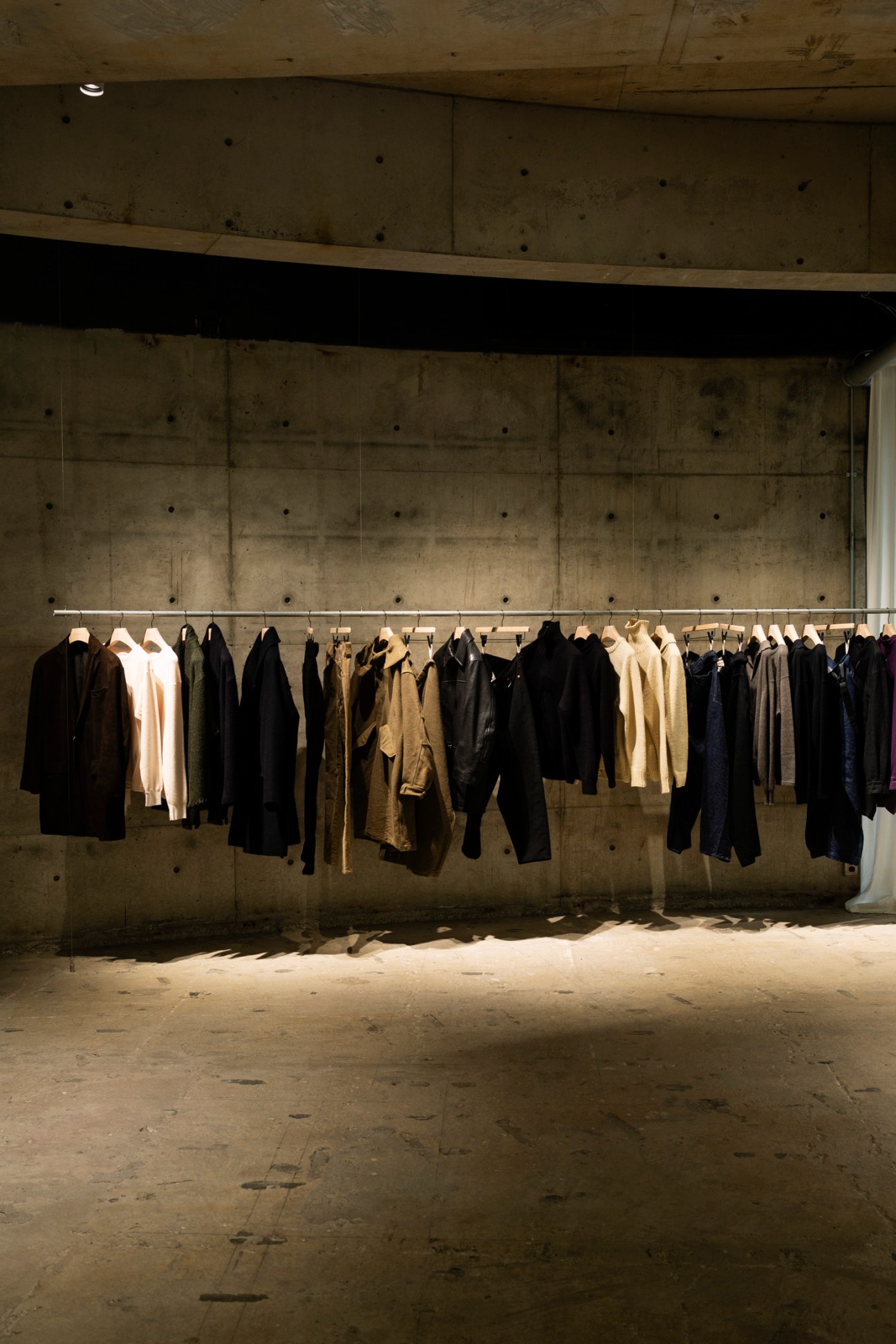 Clothing on a horizontal rail against a bare concrete wall in a minimalist retail space.