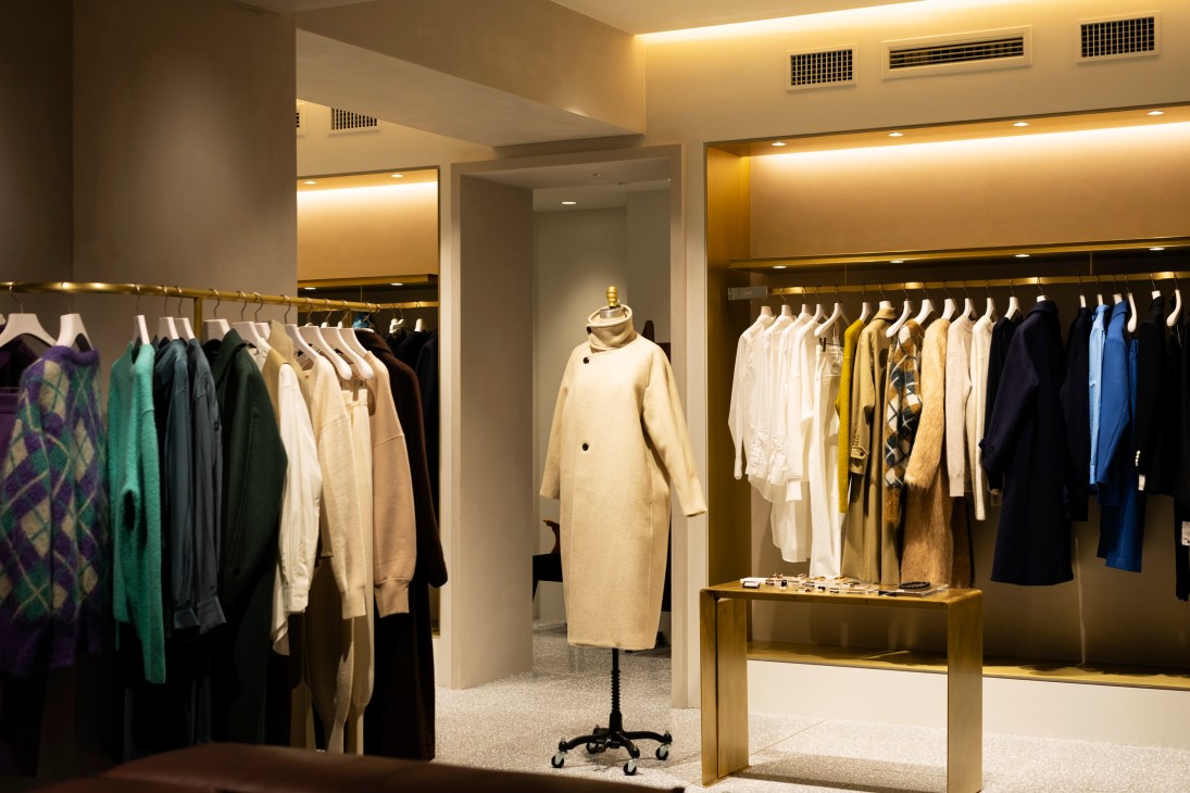 Interior of Loeff boutique in United Arrows shop with clothing displayed on brass rails and a cream coat on a dress form.
