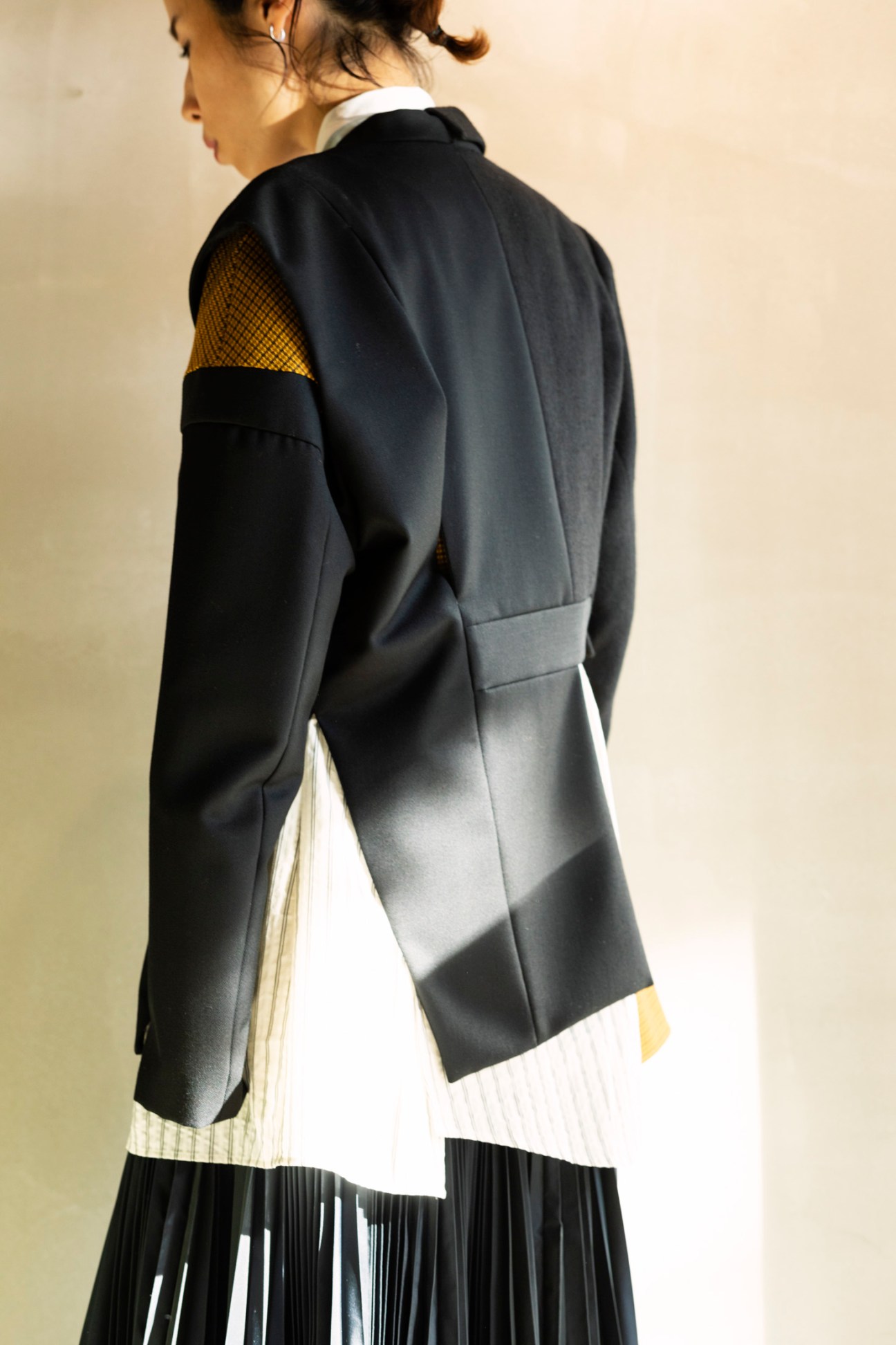 Woman wearing a navy blazer with gold and black colorblock sleeve detail over a white pleated skirt.