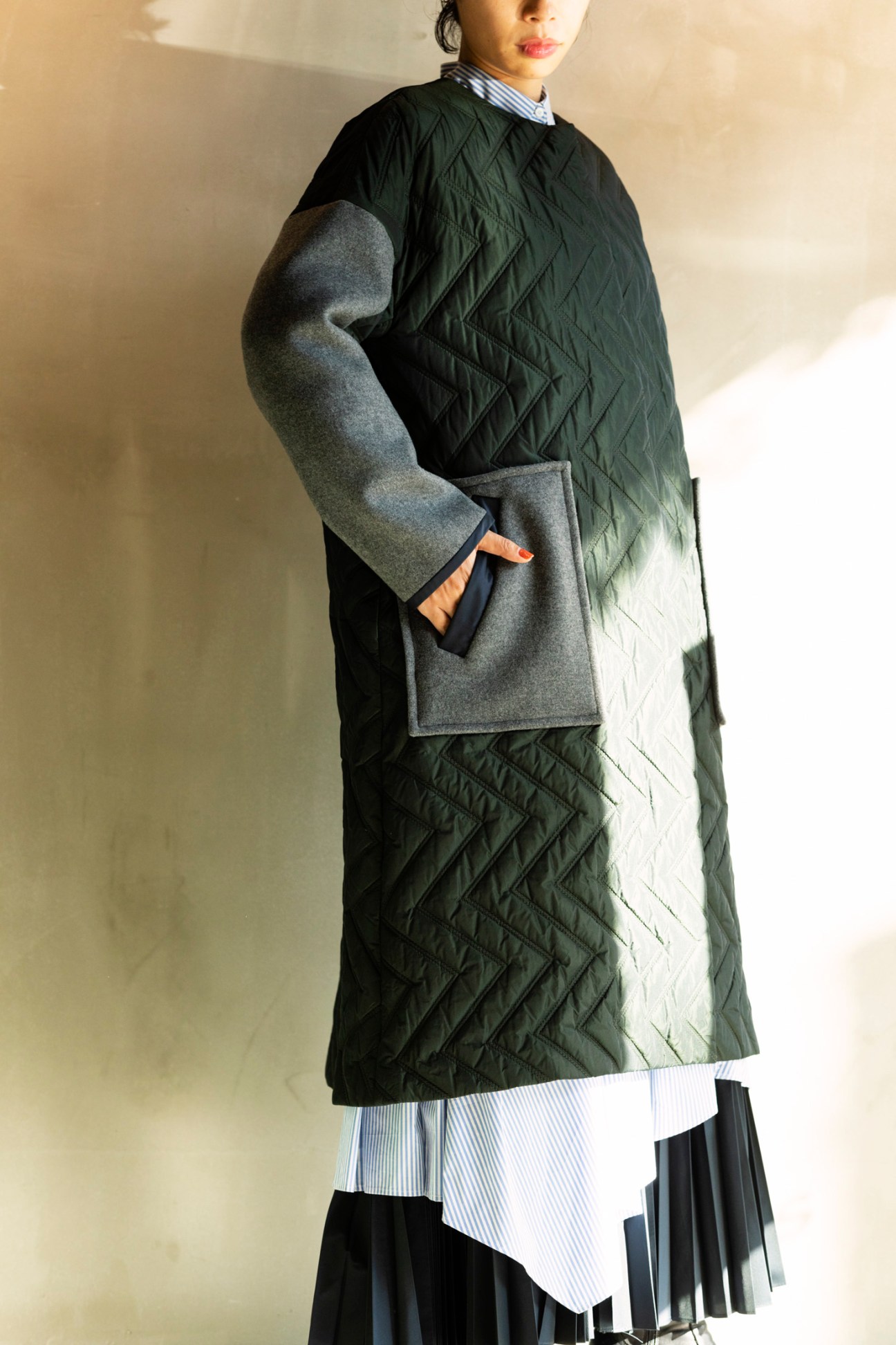 Woman wearing a black quilted jacket over a striped shirt with pleated skirt detail.