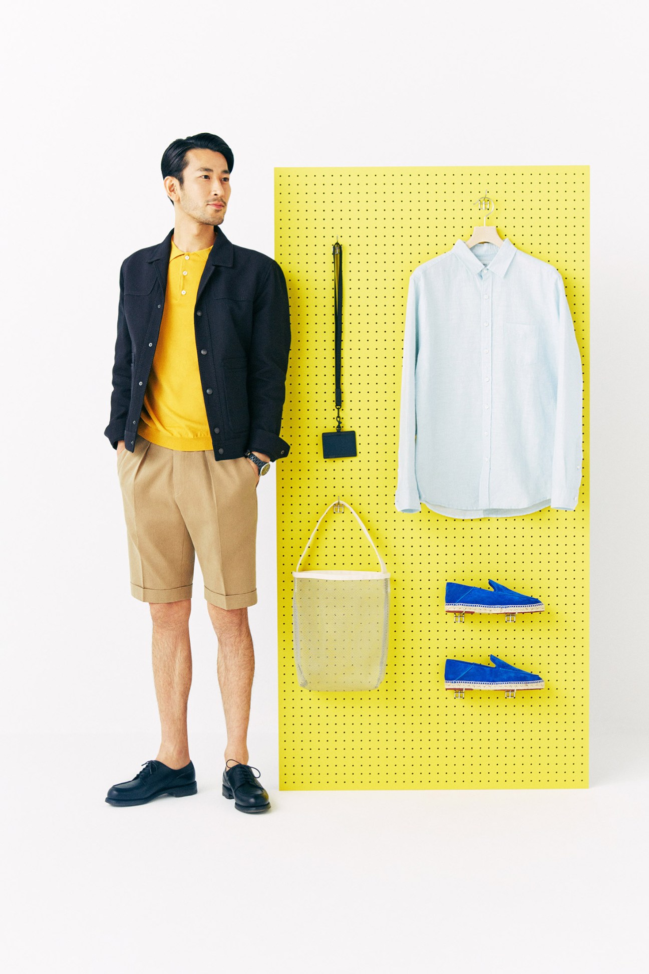 Man wearing black Bottega Veneta jacket and yellow shirt posed next to yellow pegboard displaying clothing and accessories.