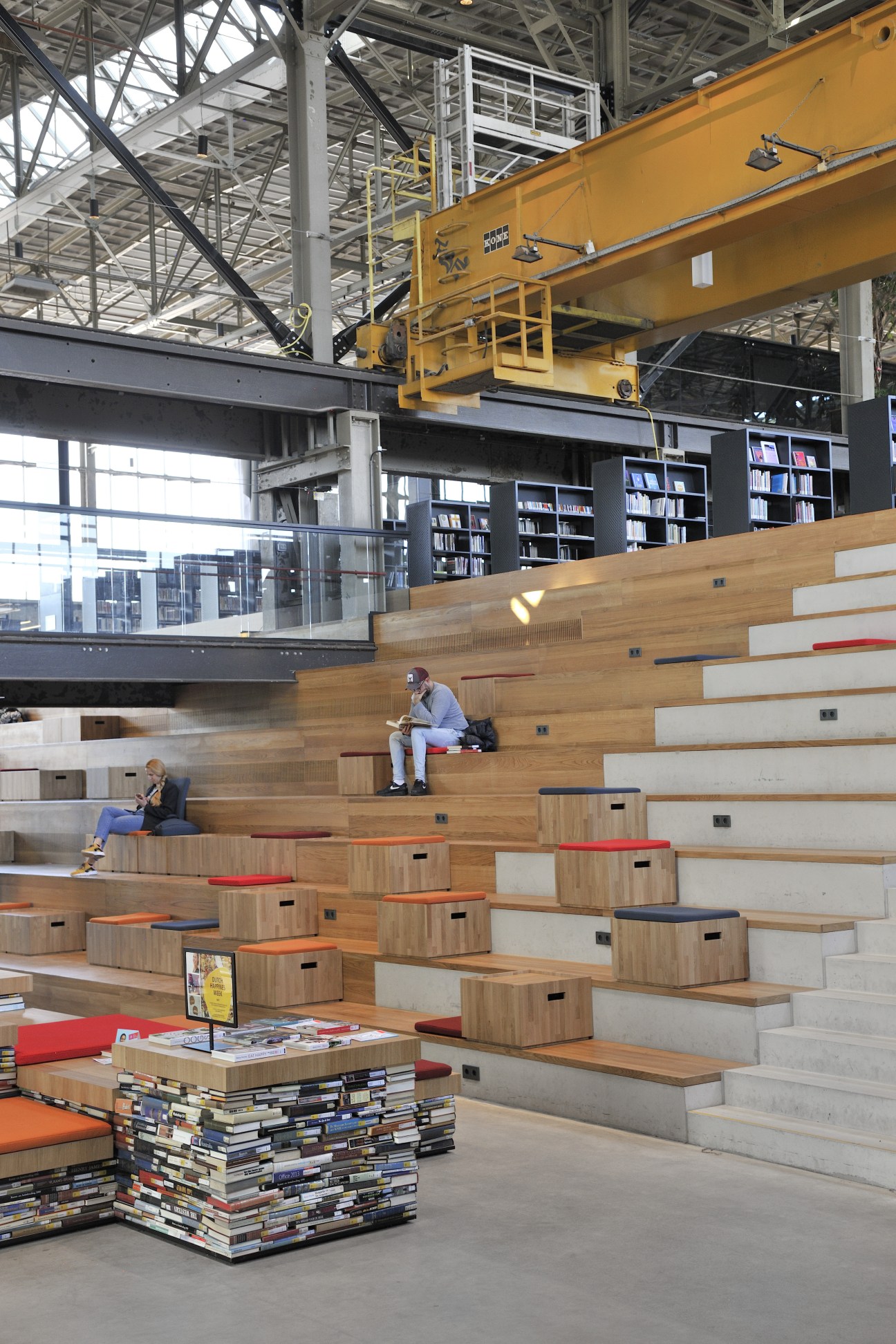 Wooden tiered steps with integrated storage cubbies and colorful cushions in an industrial warehouse space with yellow overhead crane.