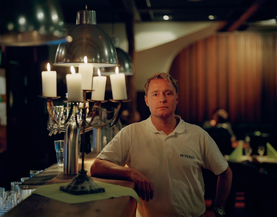 Magnus Larsson, manager and co-owner of Butler's restaurant, stands at a bar counter next to a candlelit lamp.
