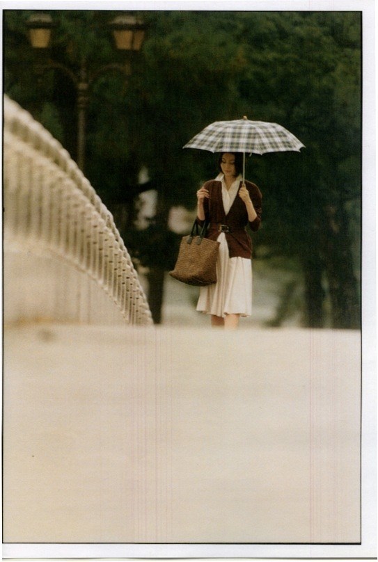 Woman holding a checkered umbrella wearing a Salvatore Ferragamo dress and Fendi cardigan in a park setting.