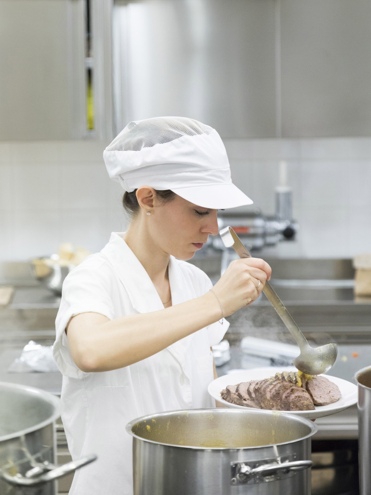 Kitchen staff member in white chef's uniform serving sliced veal at Brunello Cucinelli's company canteen