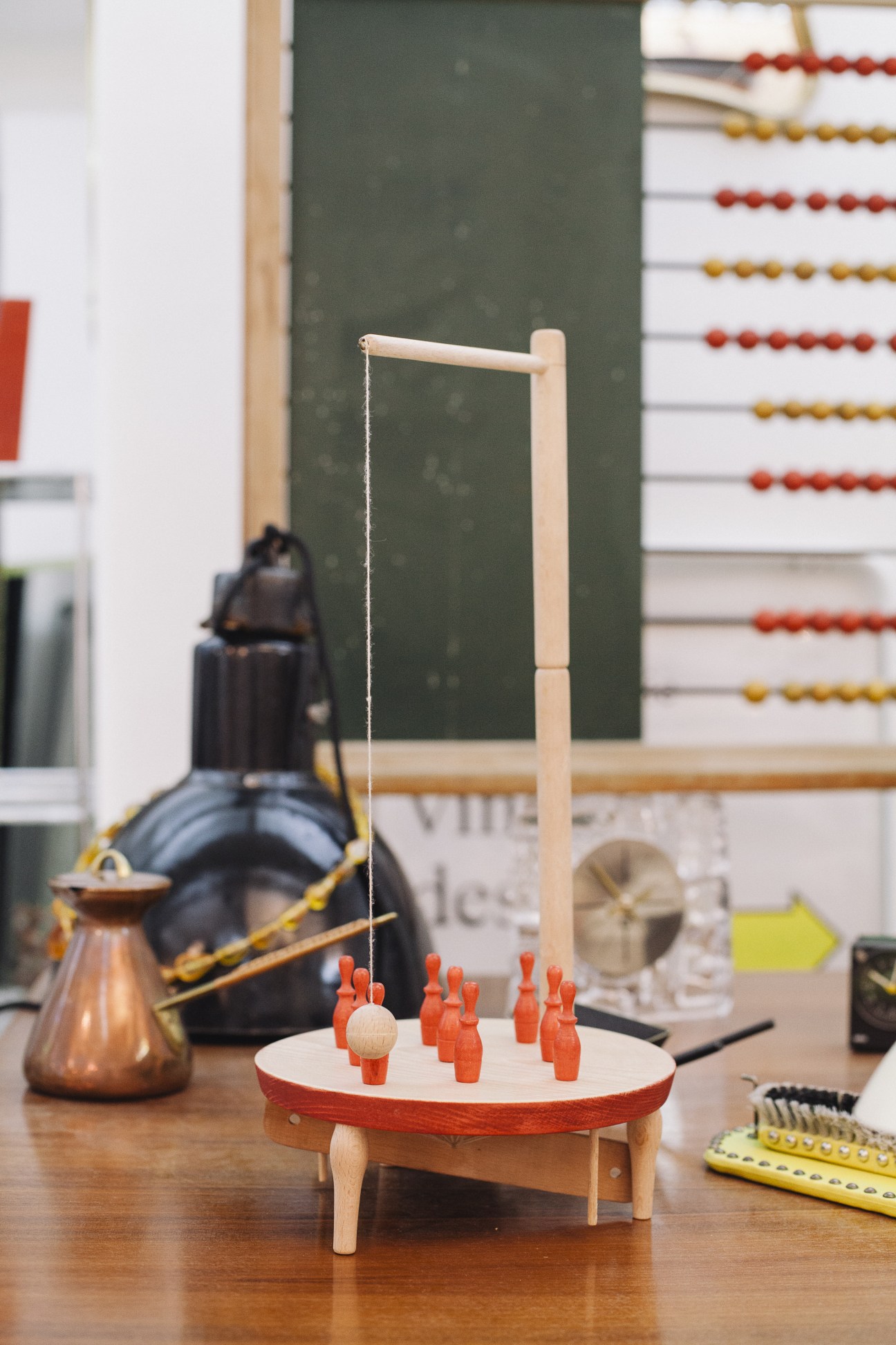 Wooden toy game with red bowling pins and dangling ball on classroom desk.