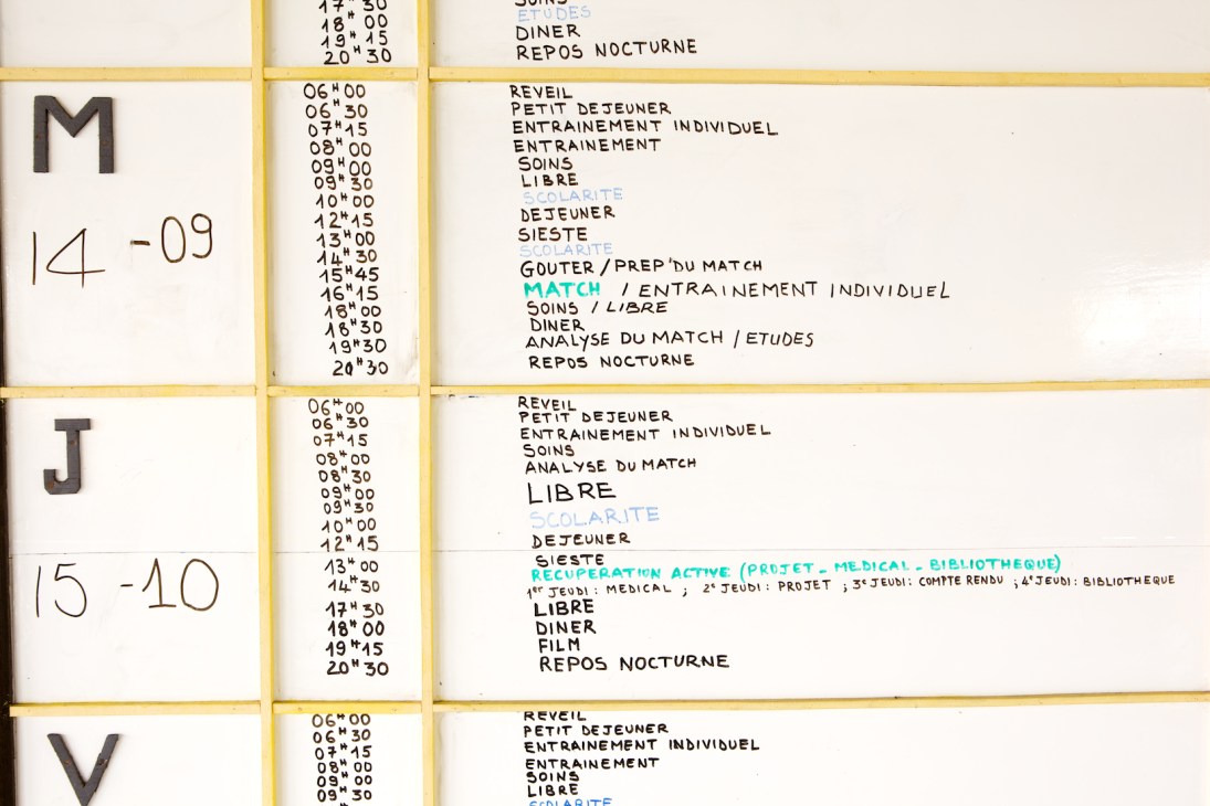 A hand-written weekly schedule in French displayed on a yellow-framed board showing daily training, classes, and activities at ASEC Mimosas academy.