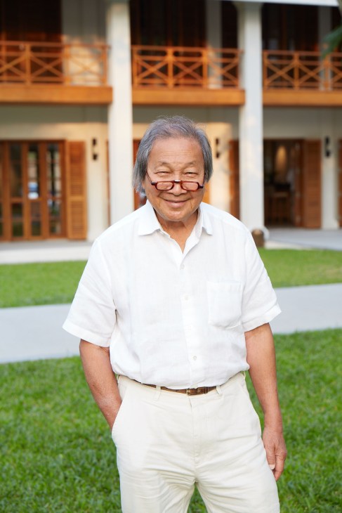 Adrian Zecha, 84-year-old Azerai owner, stands smiling in white shirt and beige trousers in front of colonial-style building.