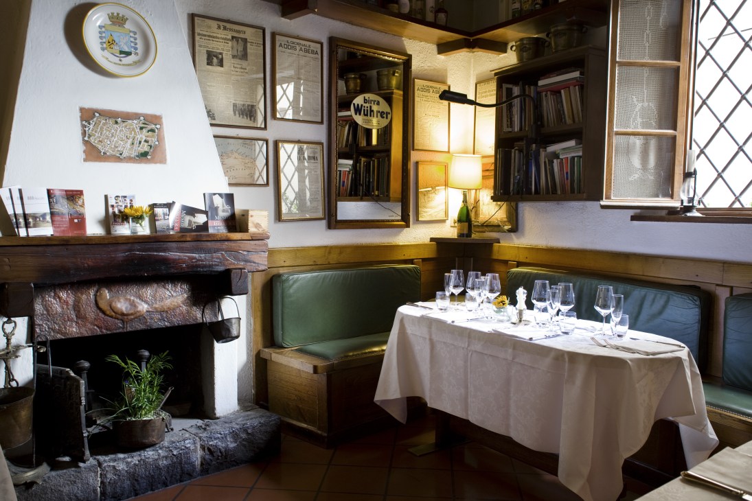 Interior of Buca di Sant'Antonio restaurant with fireplace, green banquette seating, and set dining table.