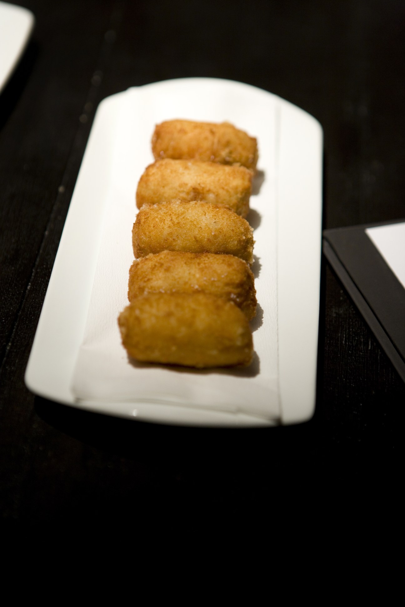 Four golden-brown croquetas de pollo arranged in a line on a white rectangular plate.