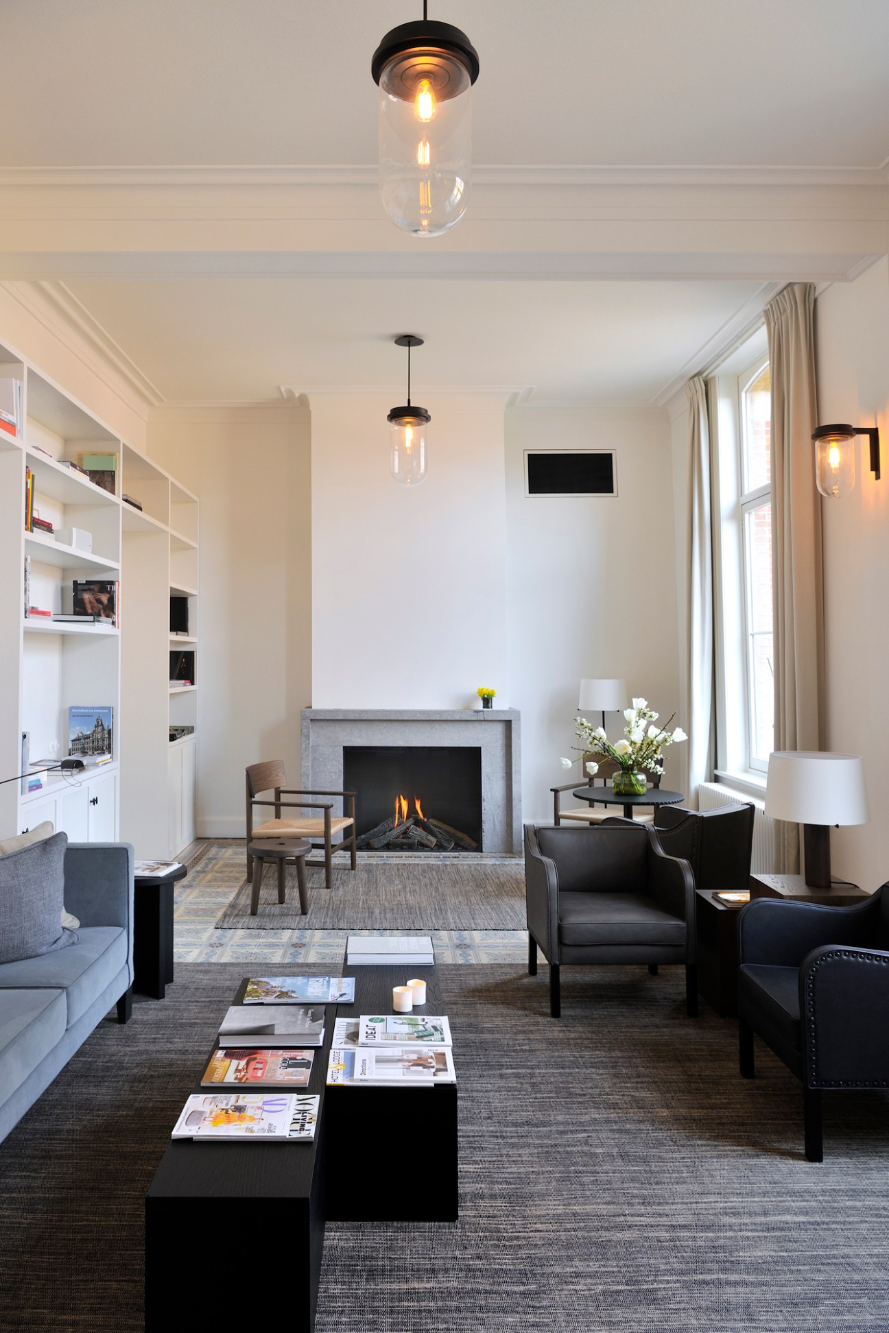 August hotel library with fireplace, pendant lights, black leather chairs, and built-in shelving.