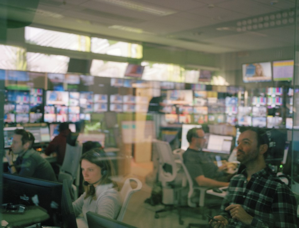Euronews control room with multiple monitors and staff working at desks under green-lit ceiling.
