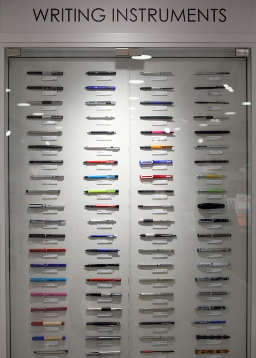 Museum display case of writing instruments organized in columns with product labels.