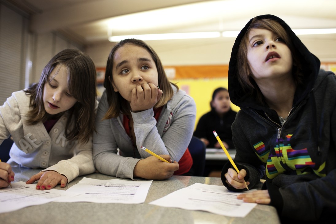 Three elementary school students studying at desks during a class lesson.