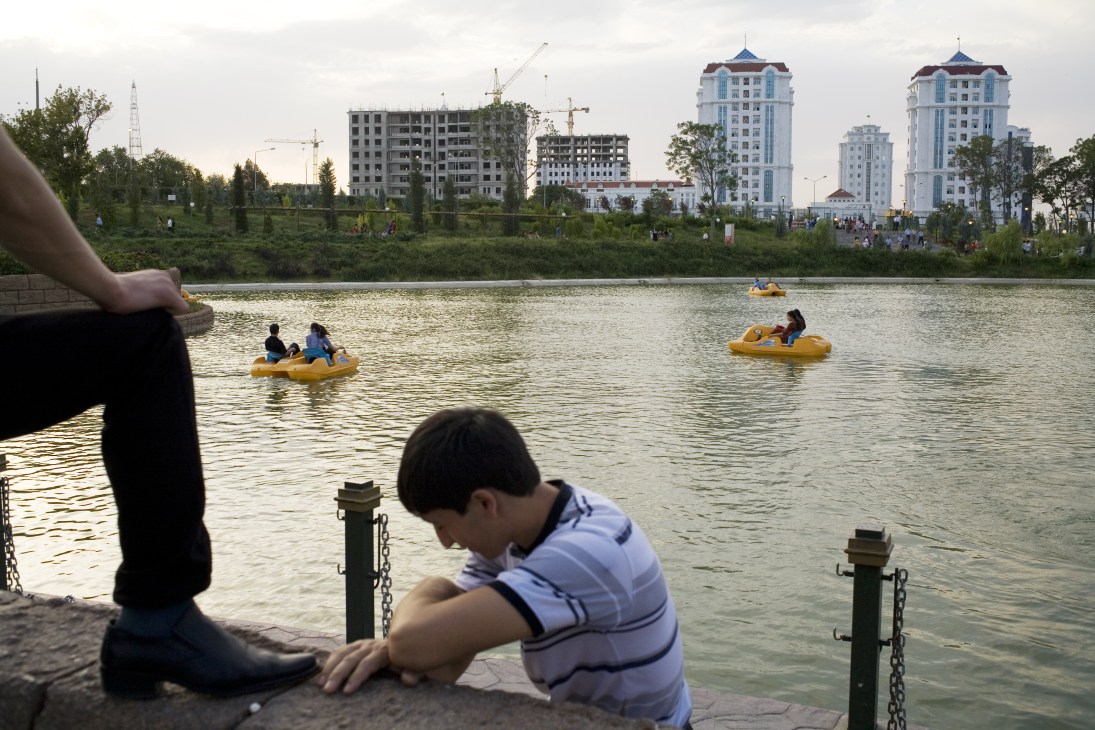 Children on yellow paddleboats in an artificial lake with modern apartment buildings behind them.