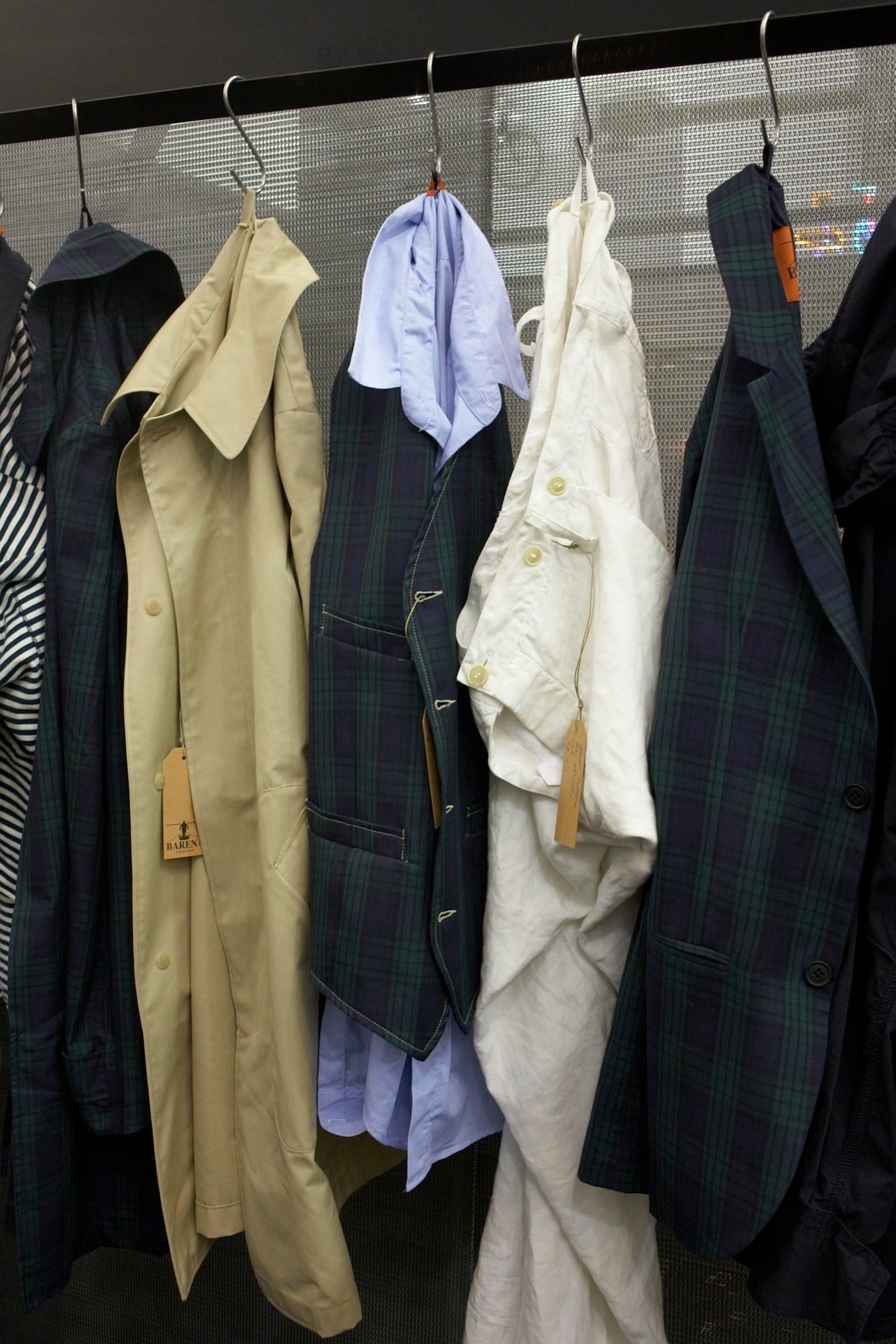Barena's fishing and hunting-inspired menswear collection displayed on hangers, featuring tailored jackets in navy plaid and cream linen.