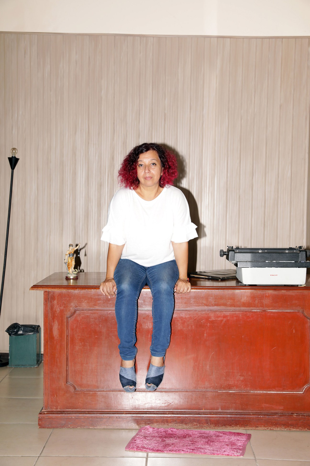 Feminist politician Lilian Soto sits on a red desk against a striped wall.