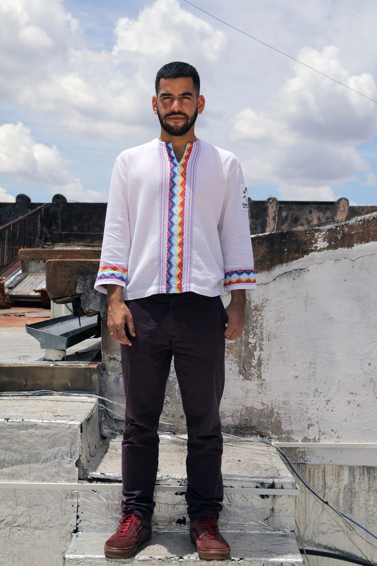 LGBT rights activist Sergio López stands on rooftop wearing white shirt with colorful geometric trim.