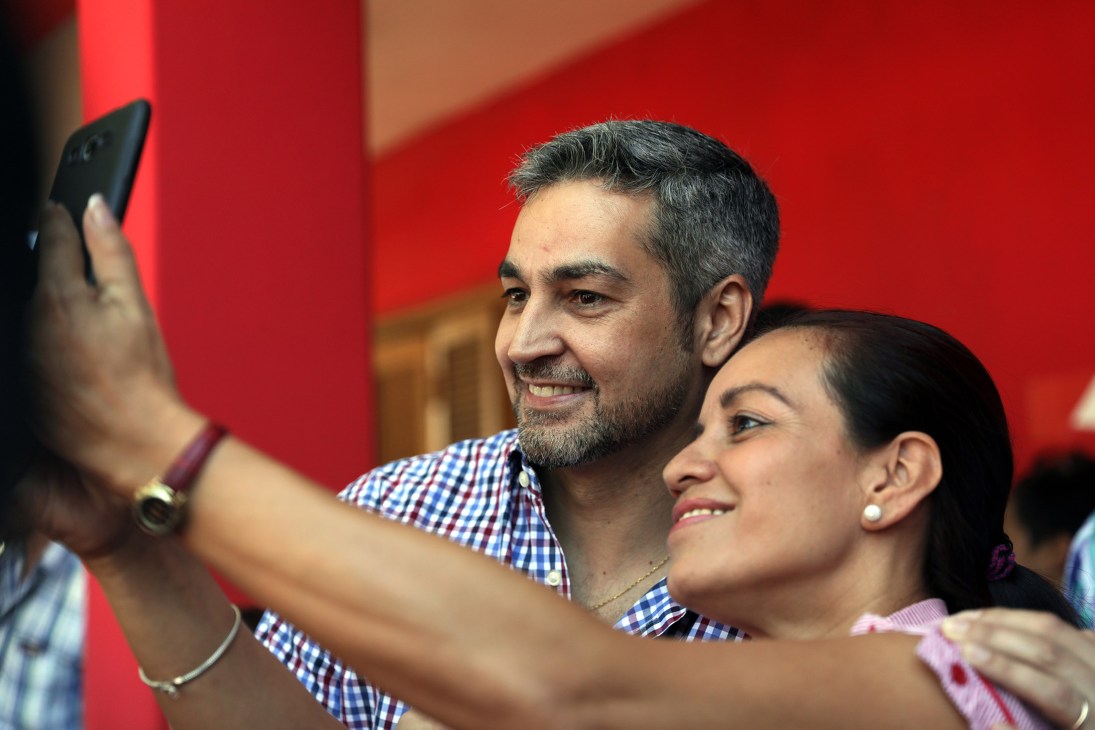 A man and woman taking a selfie together against a red wall background.