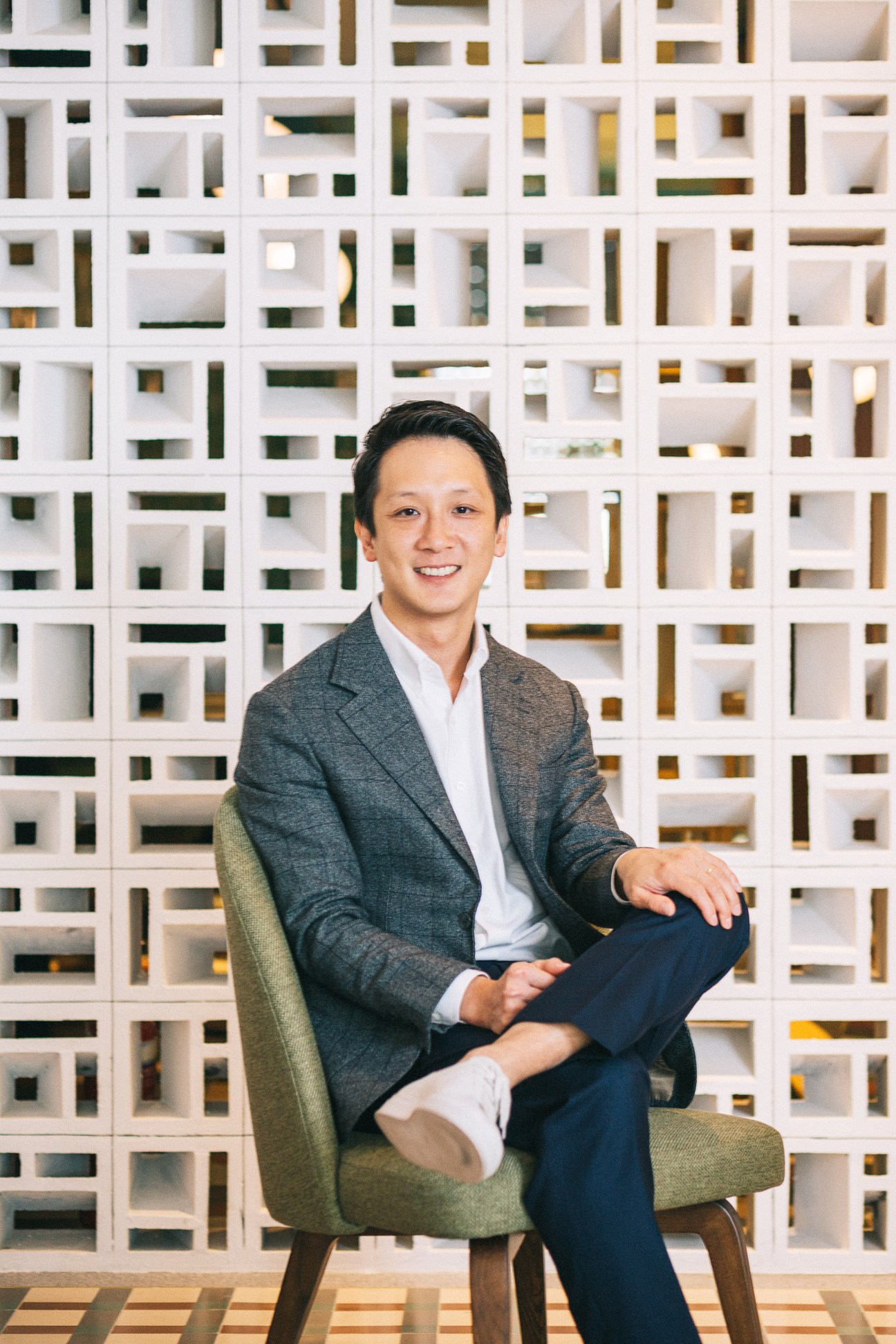 Wee Teng Wen, co-founder of Straits Clan, sits smiling in a green chair against a white latticed wall.