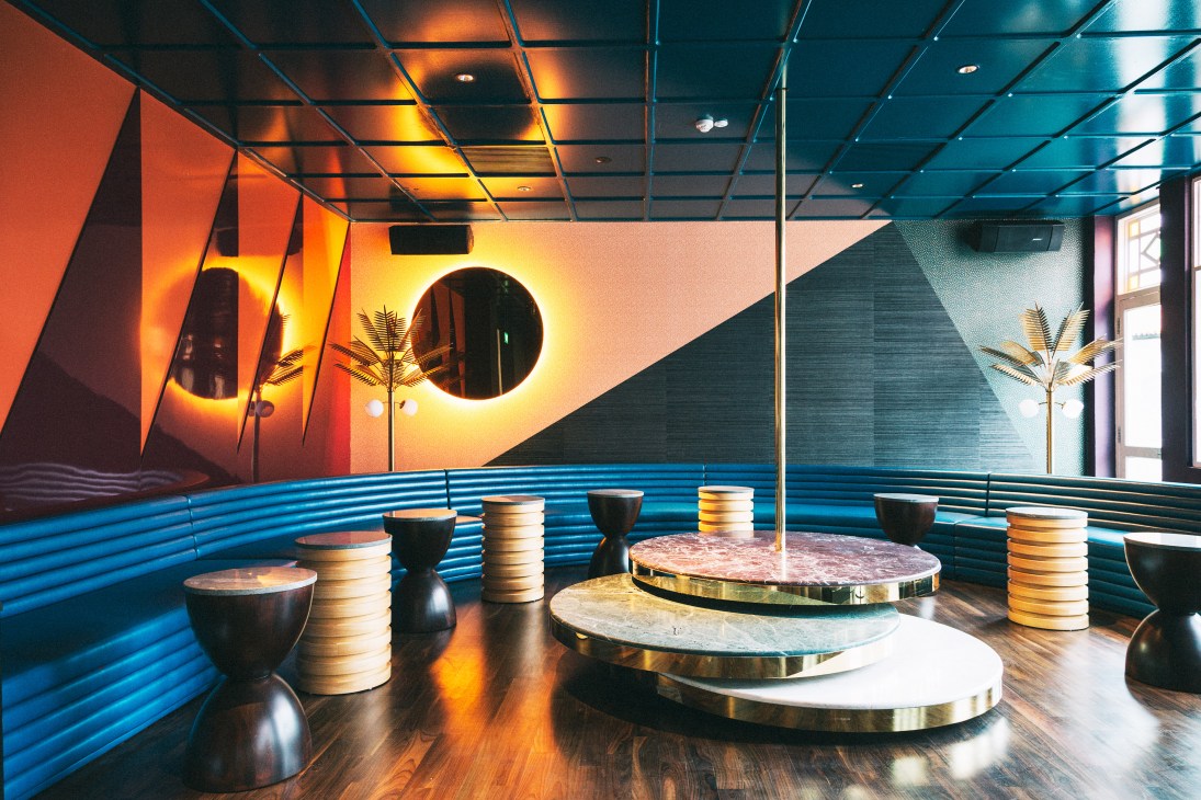 The Tropicana entertainment room at Straits Clan with blue bench seating, neon-lit circular mirrors, and modern fixtures.