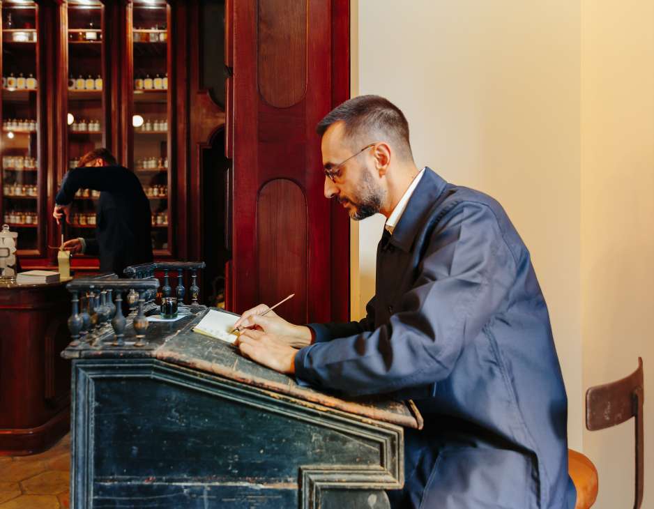 Calligrapher Bruno Gigarel writes customer names on packaging at a wooden desk in Buly 1803.