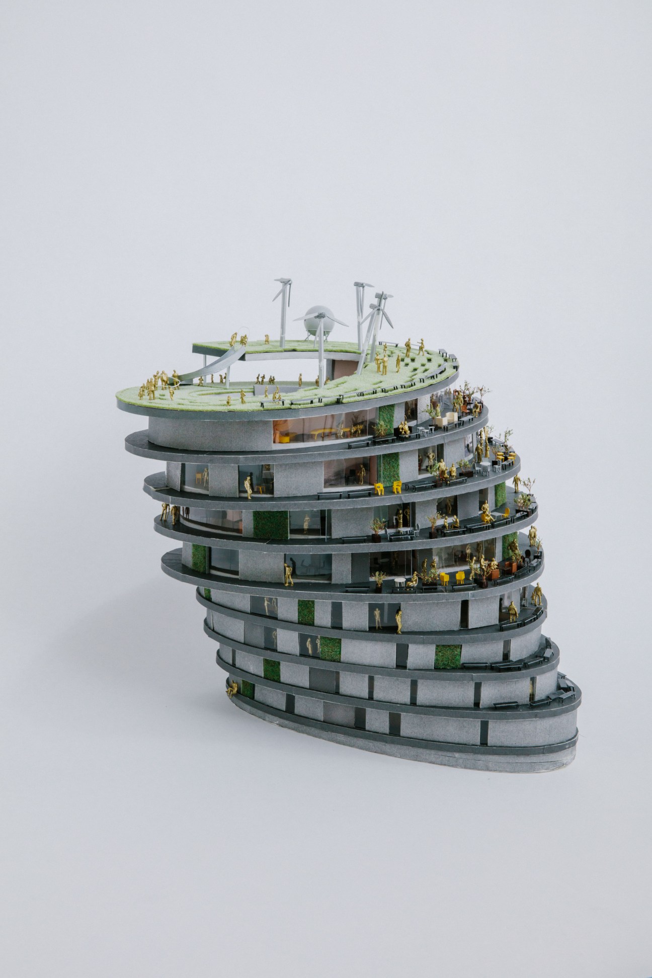 Architectural model of a spiral tower with multiple levels, green landscaping, and wind turbines on top by Hiroshi Nakamura.