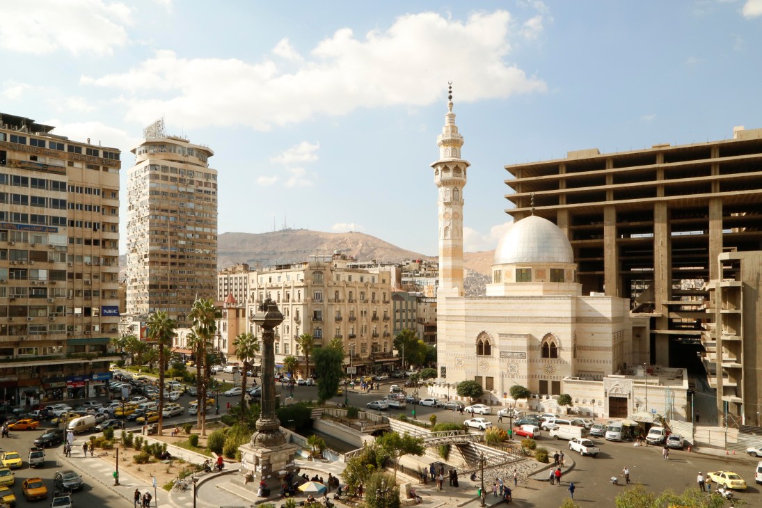 Merjeh Square in Damascus showing a mosque with minaret, modern buildings, traffic, and hills in background